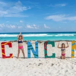 Enfant jouant devant le grand panneau coloré “Cancún” sur la plage