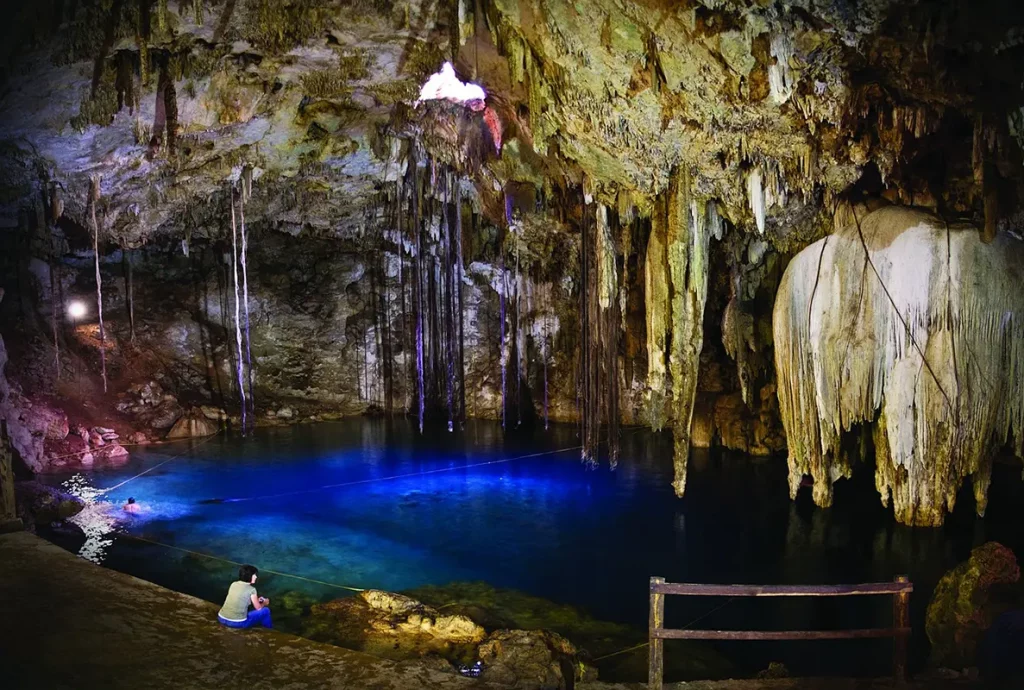 Cenote naturel dans une grotte, avec eau cristalline et rayons de lumière pénétrant depuis l’ouverture