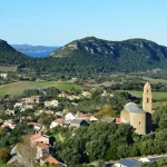 Vue panoramique d’un village corse perché, entouré de montagnes avec l’océan à l’horizon