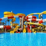 Grand parc aquatique avec piscine et nombreux toboggans colorés sous un ciel bleu